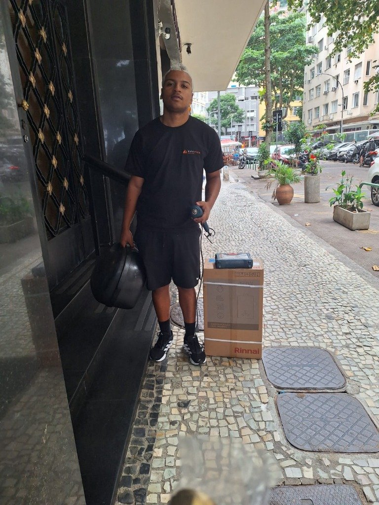 Técnico da equipe Gás Fixe na calçada com caixa de aquecedor Rinnai